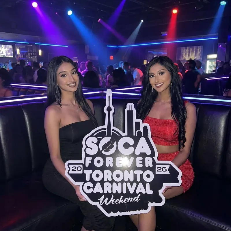 Two friends at a Soca Forever night party holding the Toronto Carnival sign