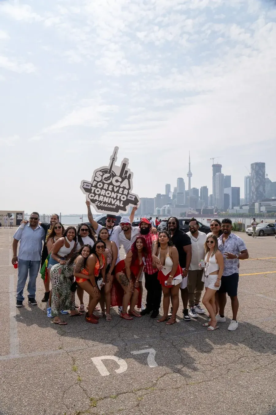 Crowd of past Soca Forever attendees holding the Toronto Carnival sign with the downtown Toronto skyline behind them